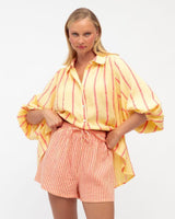 Woman wearing a yellow and orange striped cotton set with a button-down balloon-sleeve shirt and drawstring shorts.