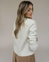 Woman wearing a cream-colored, structured boucle Harmony Jacket with long sleeves, viewed from the back.