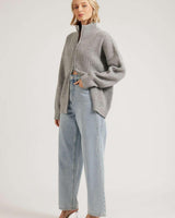 Model wearing a grey ribbed knit zip-through cardigan with a high neck, styled with light wash denim jeans.