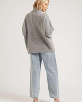 Woman wearing a grey ribbed zip-through cardigan with a high neck, paired with light wash denim jeans.
