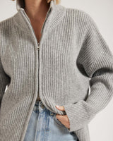 Grey ribbed zip-through cardigan with a high collar, worn over light wash blue jeans.