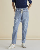 A person standing against a beige background, wearing blue straight leg jeans with an elasticated waist and drawcord, paired with a navy top and white sneakers.
