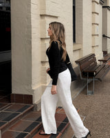 Woman wearing high-waisted white textured jersey pants with a straight-leg cut and black long-sleeve top.