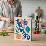 House of Holabox Adriatico cookbook featuring colorful Mediterranean food illustrations on a kitchen counter
