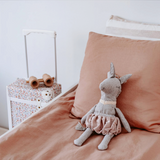 House of Holabox Alice Unicorn soft toy in grey wool blend with a gold shimmer bubble skirt sitting on a bed