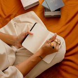 House of Holabox Alta pocket mindfulness journal being used for writing on a burnt orange background