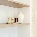 House of Holabox saide amber glass wood wick candle and reed diffuser set on a textured tray on a wooden shelf