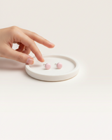 House of Holabox handmade baby pink resin round stud earrings resting on a small white tray with a hand reaching out