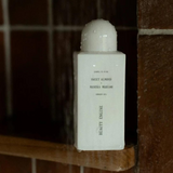 House of Holabox Beauty Engine Sweet Almond and Manuka Honey shower oil bottle in a wet, tiled shower setting.