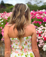 House of Holabox Beccy strapless maxi dress with pink floral print, worn by a woman with a pearl headband in a garden