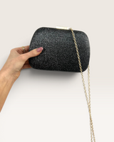 House of Holabox Mascara evening clutch in black glitter with a gold chain strap and secure buckle closure.