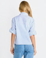 Back view of a woman wearing a House of Holabox blue and white striped cropped poplin shirt with cuffed sleeves.