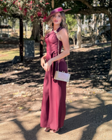 Model wearing a House of Holabox cherry chocolate jumpsuit with asymmetric neckline, gold buckle, and waist tie.