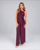 House of Holabox cherry chocolate jumpsuit with asymmetric neckline, gold buckle, and waist tie on a model.