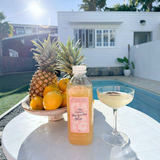 House of Holabox Margarita Margarita classic mix bottle next to a cocktail glass and pineapples by a pool