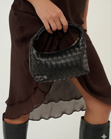 House of Holabox Cleo black woven vegan leather handbag with an adjustable top handle held by a model