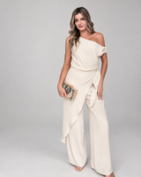 Model wearing a House of Holabox cream one-shoulder jumpsuit with draped waist tie and wide-leg trousers.