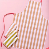 House of Holabox Ecology Porto Lola almond striped kitchen apron with matching oven mitts on a pink background