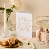 House of Holabox greeting card with gold foil Let There Be Cake & Bubbles text, styled with macarons and champagne.