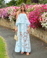 House of Holabox icy blue sheer floral tiered midi dress with adjustable straps worn by a woman near pink flowers