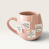 House of Holabox Inspirational Tea Co. pyramid teabags with uplifting quotes hanging from a soft pink ceramic mug