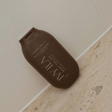 House of Holabox Ivy Ila Black Raspberry and Vanilla sugar body polish in a brown squeeze bottle on a stone surface.