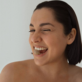 House of Holabox Ivy Ila hand cream model winking while holding a lychee fruit in her mouth against a white background
