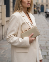 House of Holabox Izoa Brianna gold pleated hard-frame clutch held by a woman in a cream blazer on a city street.