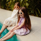 Two girls wearing House of Holabox Little Drop kids sunglasses with UV400 protection while sitting by a pool.