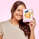 A smiling woman holding a box of House of Holabox Lula self-warming body patches against a soft pink background.