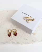 House of Holabox Lustre & Sage red and white heart earrings with 18K gold plating displayed on a stone surface.
