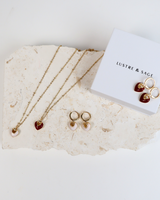 House of Holabox Lustre & Sage heart necklaces and earrings in red and white with gold plating on a stone display.