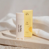 House of Holabox Stray Willow Mango Sorbet lip balm stick with its yellow cardboard packaging on a stone tray.
