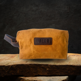 House of Holabox Valor mustard waxed canvas toiletry bag with leather trim and handle on a stone surface
