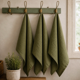 House of Holabox olive green French linen tea towels hanging on a rustic wall rack in a kitchen setting