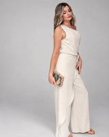 House of Holabox one-shoulder cream jumpsuit with draped waist tie and wide legs worn by a blonde model