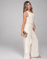 House of Holabox one-shoulder cream jumpsuit with draped waist tie and wide legs worn by a blonde model