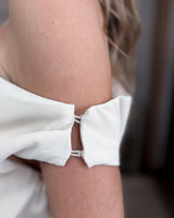 House of Holabox white one-shoulder jumpsuit featuring draped fabric detail and delicate strap connectors on the arm.