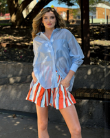 House of Holabox model wearing a pale blue oversized lyocell-blend shirt tucked into striped shorts outdoors