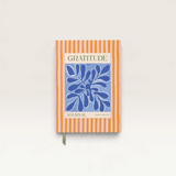 House of Holabox Papier gratitude journal with orange and pink stripes and a blue botanical cover illustration