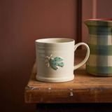 House of Holabox Robert Gordon stoneware mug in dove featuring a hand-painted festive bird motif on a wooden table.