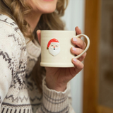 House of Holabox Robert Gordon stoneware mug with a hand-painted Santa motif held by a person in a festive sweater