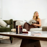 House of Holabox saide. large amber glass soy candle with wood wick burning on a marble table in a cozy living room