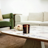 House of Holabox saide. large amber glass soy candle with a wood wick sitting on a marble coffee table in a living room