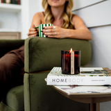 House of Holabox saide. amber glass wood wick candle burning on a coffee table book in a cozy living room setting
