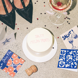 House of Holabox Salty Melon Prints SALUT mini greeting card next to a small cake, cocktail, and decorative confetti.