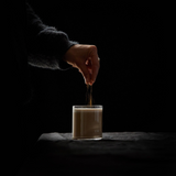 House of Holabox Somage 9 Spice Honey Fresh Chai being sprinkled into a glass of creamy chai tea on a dark table.
