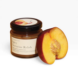 House of Holabox Spicy Nectarine Relish in a glass jar next to a fresh sliced nectarine on a yellow surface.