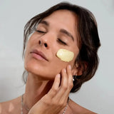 A woman applying the House of Holabox Stray Willow Golden Glow clay facial mask to her cheek for a radiant complexion.
