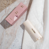 House of Holabox Stray Willow strawberry lip balm tube and pink packaging box on a textured surface